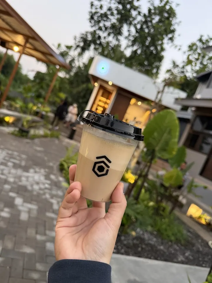An iced coffee in a Gimbo-branded cup held up in the courtyard at dusk.