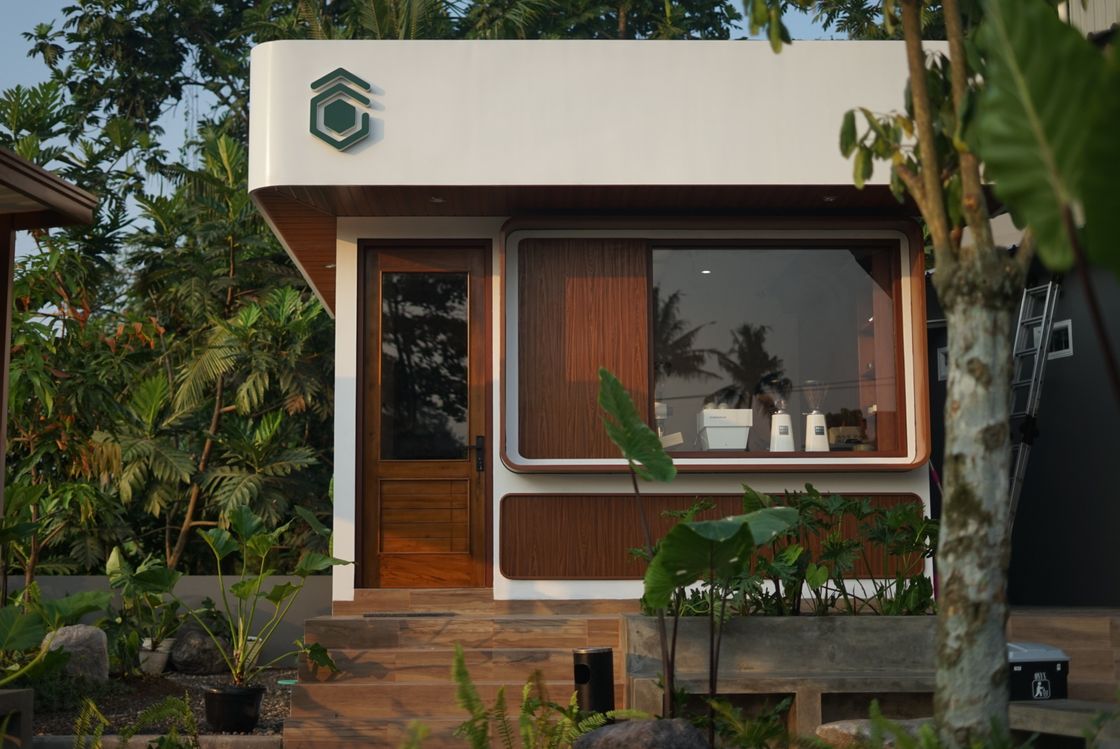 Kedai Kopi Gimbo at golden hour — a white pavilion with a warm timber door and window, surrounded by tropical greenery.